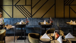 A restaurant interior with a modern design, featuring a blue cushioned bench seating, dark wooden tables, and green upholstered chairs. - Hotel Porta Cite (Maasmechelen)