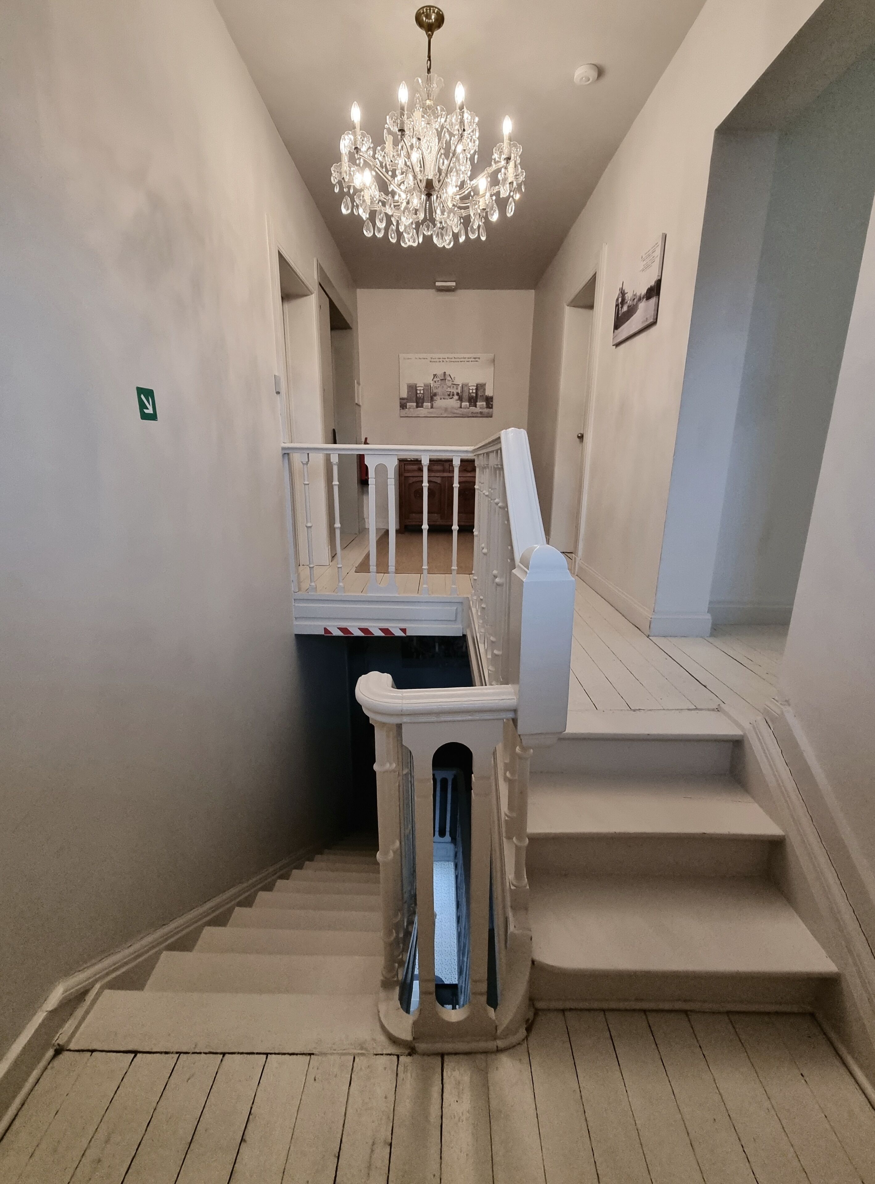 Eine Treppe mit weißer Geländer, einem Chandelier und einem gerahmten Bild an der Wand.