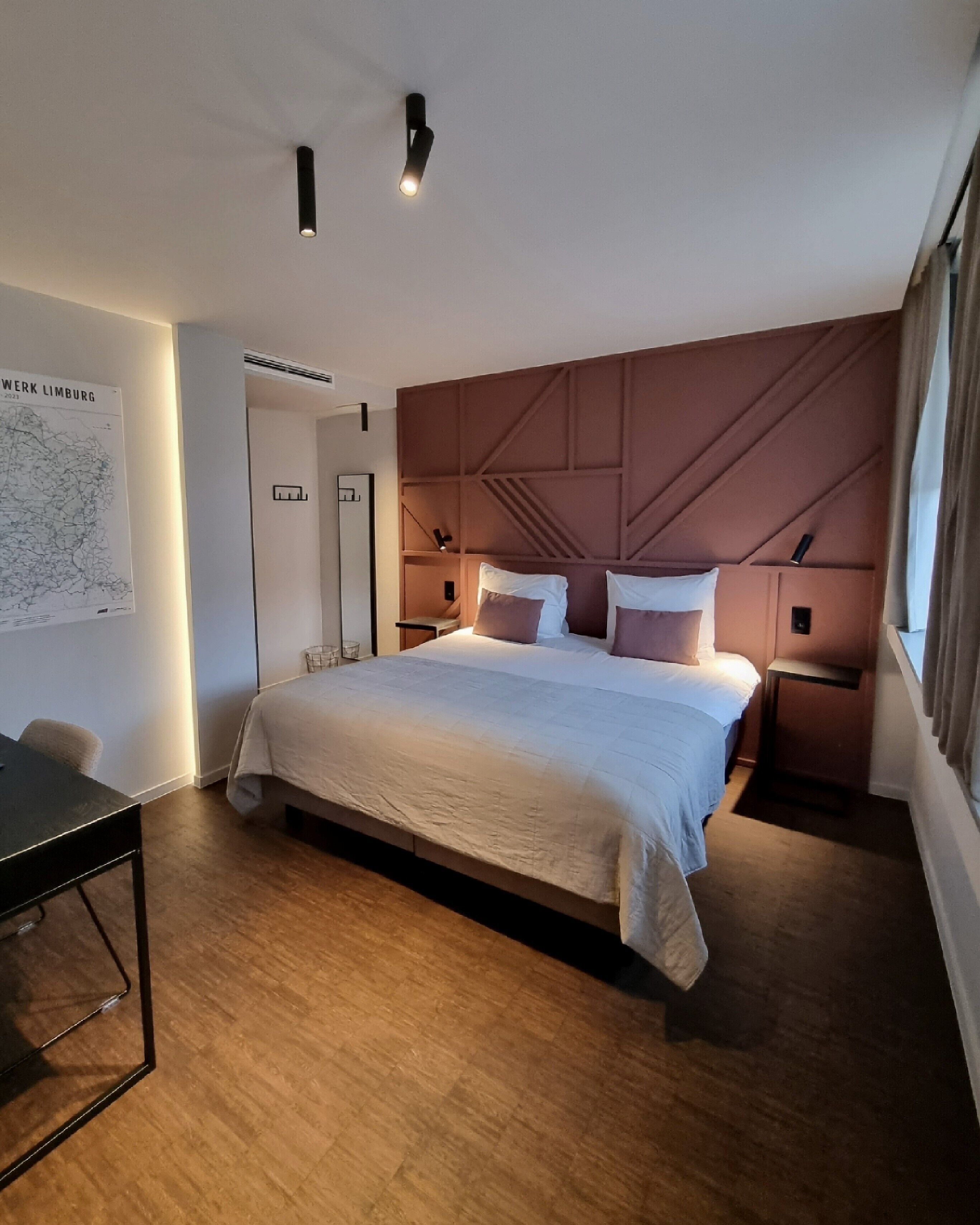 Una habitación de hotel moderna con una cama grande, un escritorio, un mapa en la pared y vistas a la ciudad.