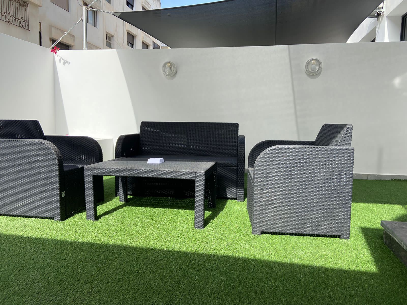 An outdoor patio with wicker furniture, including a table and two chairs, set on artificial grass.