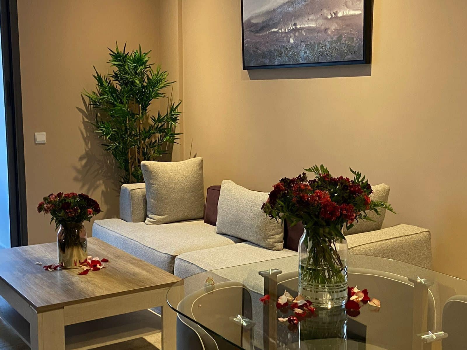A modern living room with a sofa, two side tables, a glass coffee table, and a potted plant.
