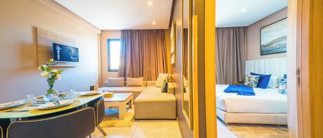 A hotel room with a dining area, a sofa, a bed, and a TV.