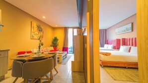 A modern hotel room with a bed, a dining area with a table and chairs, a painting on the wall, and a view of the outside. - Atlas-Résidence By Rent-Inn (Rabat)