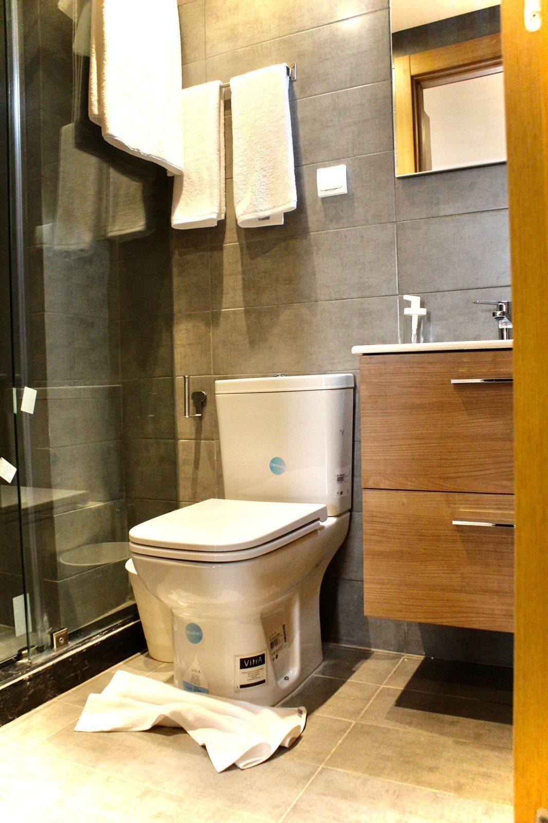 Une salle de bain moderne équipée de toilettes, d’une douche à parois de verre et d’un meuble-lavabo en bois avec un miroir.