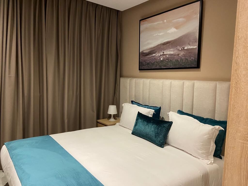 A hotel room with a large bed, a headboard, a nightstand with a lamp, and a painting on the wall.