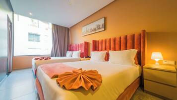 A hotel room with two beds, a cityscape painting, a lamp, and a view of buildings outside.