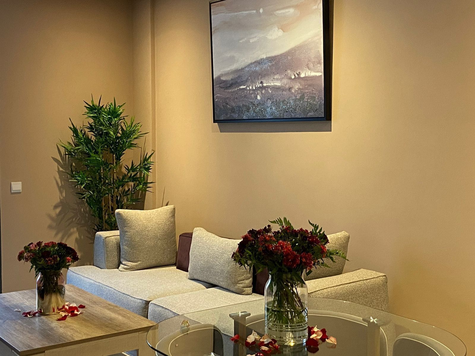 Un salon avec un canapé, deux vases de fleurs, une table basse en verre et un tableau au mur.