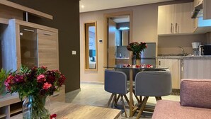 A modern kitchen with a dining area, a small table with a vase of flowers, and a sofa. - Atlas-Résidence By Rent-Inn (Rabat)