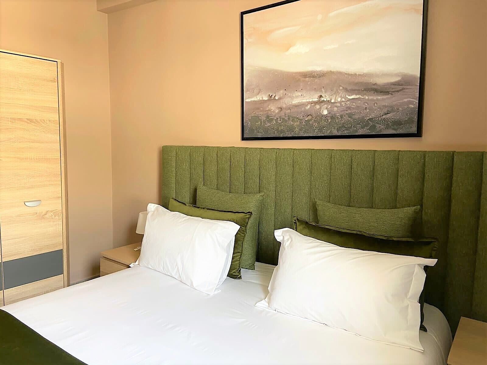 Une chambre d’hôtel avec un lit, deux oreillers, une table de chevet et un tableau encadré au mur.