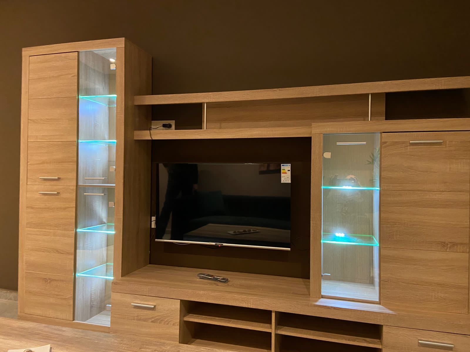 A wooden TV stand with a flat-screen TV, multiple drawers, and illuminated shelves.