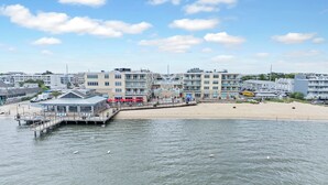 Un hôtel situé sur la côte, doté d’une jetée s’avançant dans l’eau, d’une plage aménagée avec des parasols et offrant une vue sur la mer.