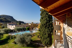 A view of a pool area with lounge chairs, a large tree, and a building with balconies. - Residence Rustico (Garda)