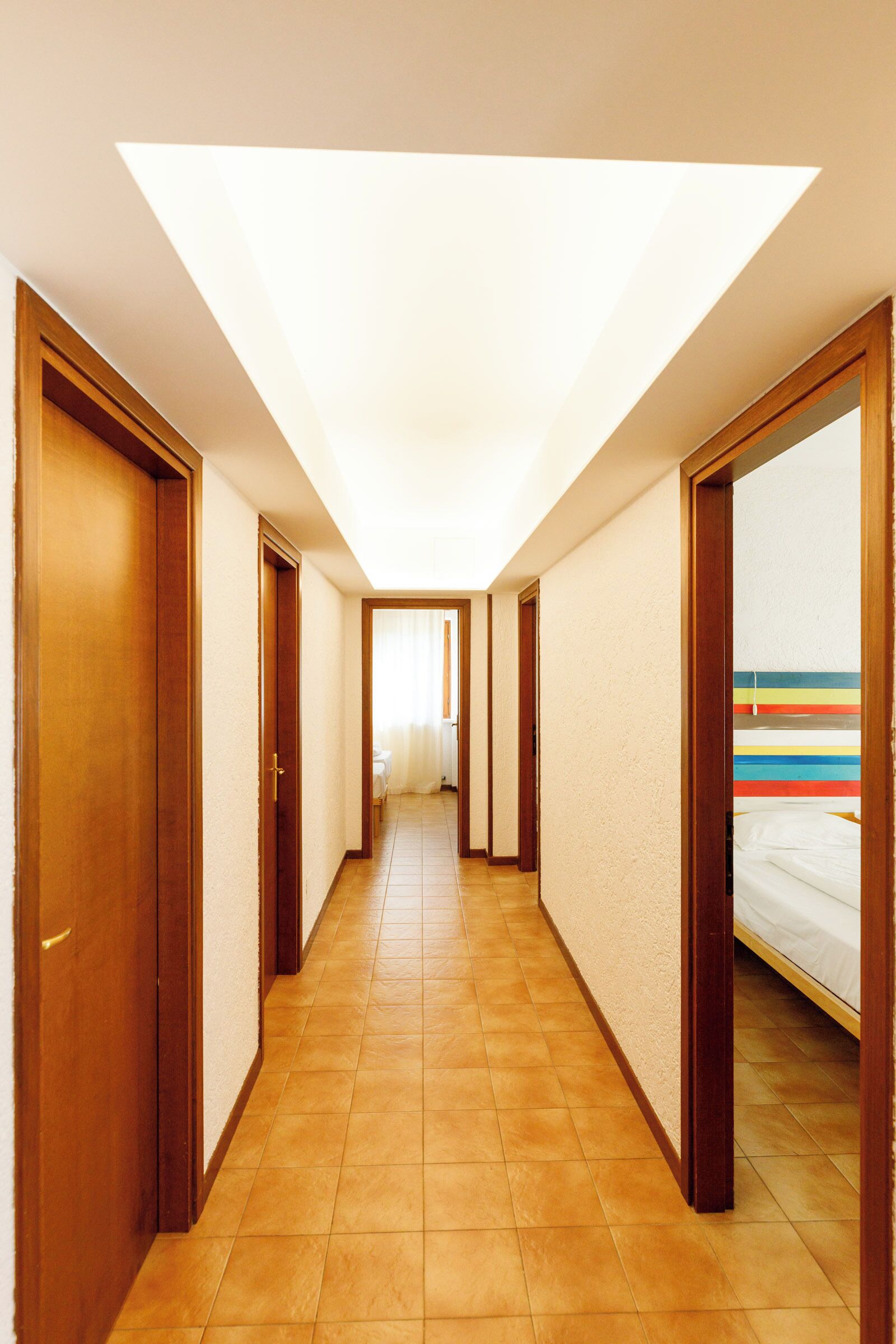 Ein Hotelgang mit Holztüren, einem Fliesenboden und Blick auf einen Raum mit Bett und farbenfroher Streifenwand.