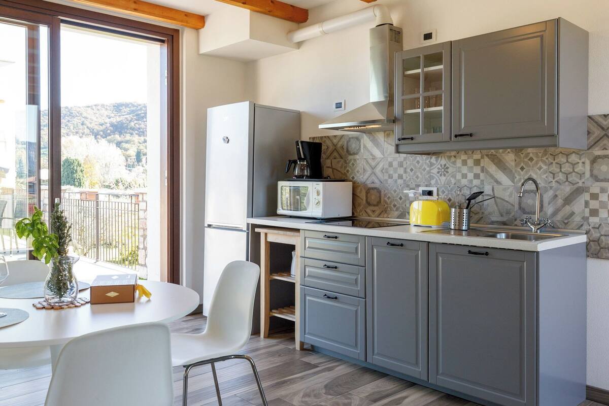 A modern kitchen with grey cabinets, a white refrigerator, and a yellow toaster. There is a dining table with white chairs and a potted plant.