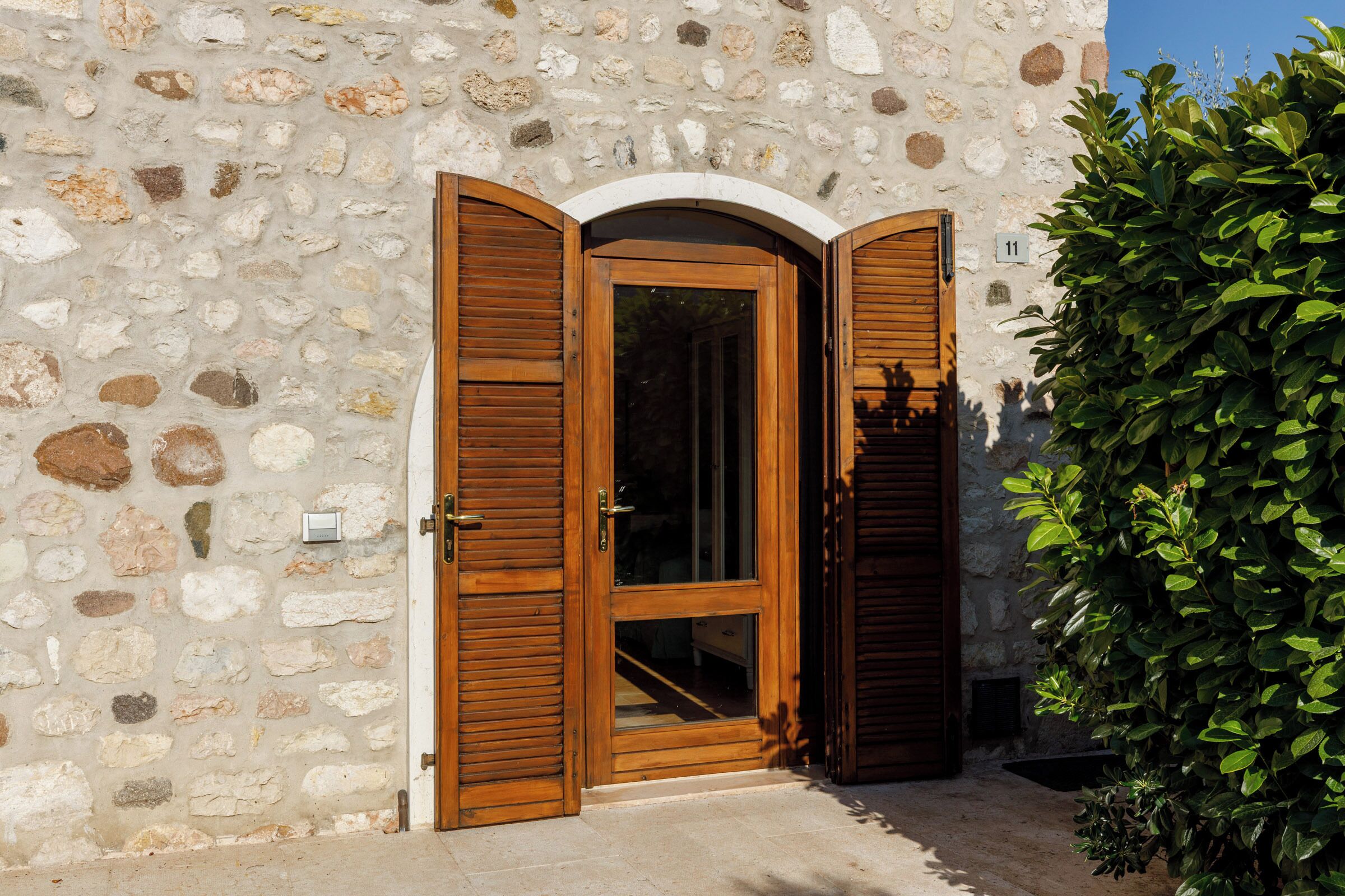 A stone building with a wooden door and shutters, a small window, and a number '11' sign.