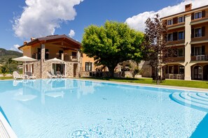 A swimming pool with lounge chairs, a stone building, and a tree. - Residence Rustico (Garda)