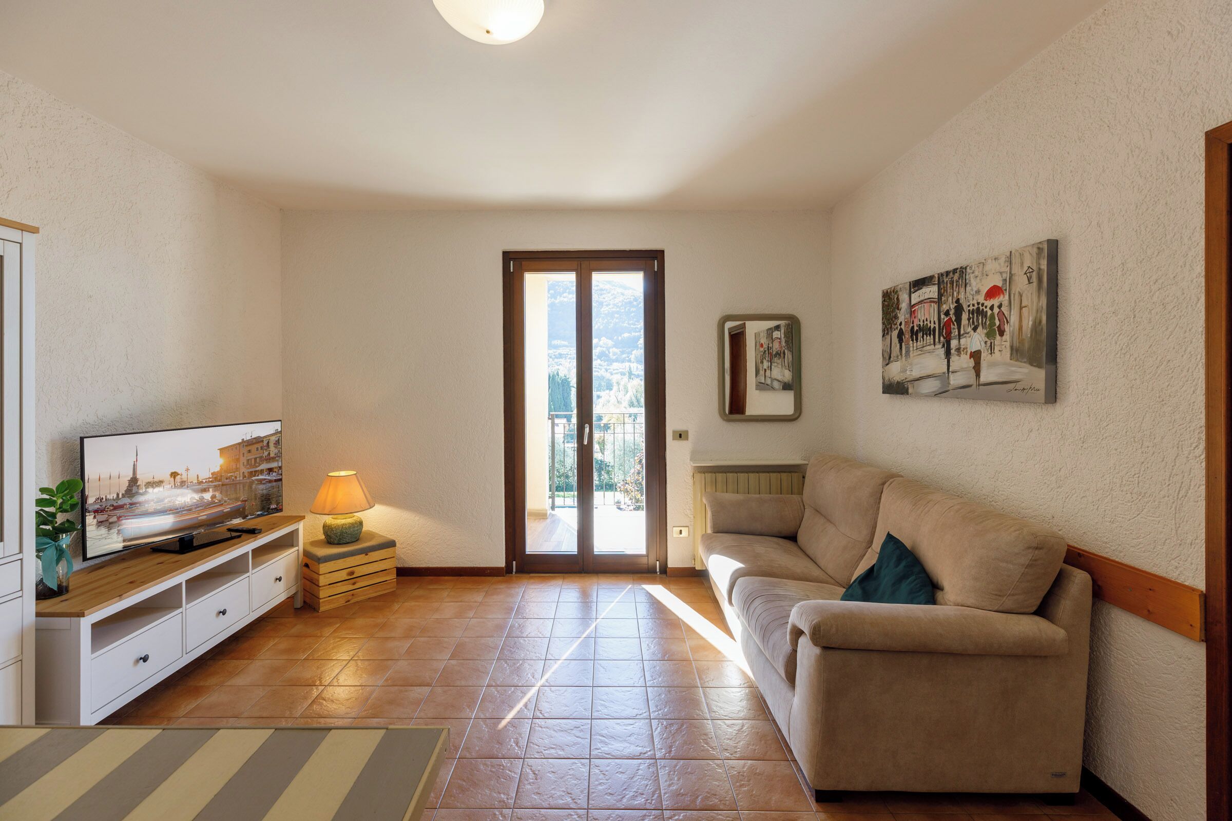 A living room with a television, a sofa, a lamp, and a painting on the wall.