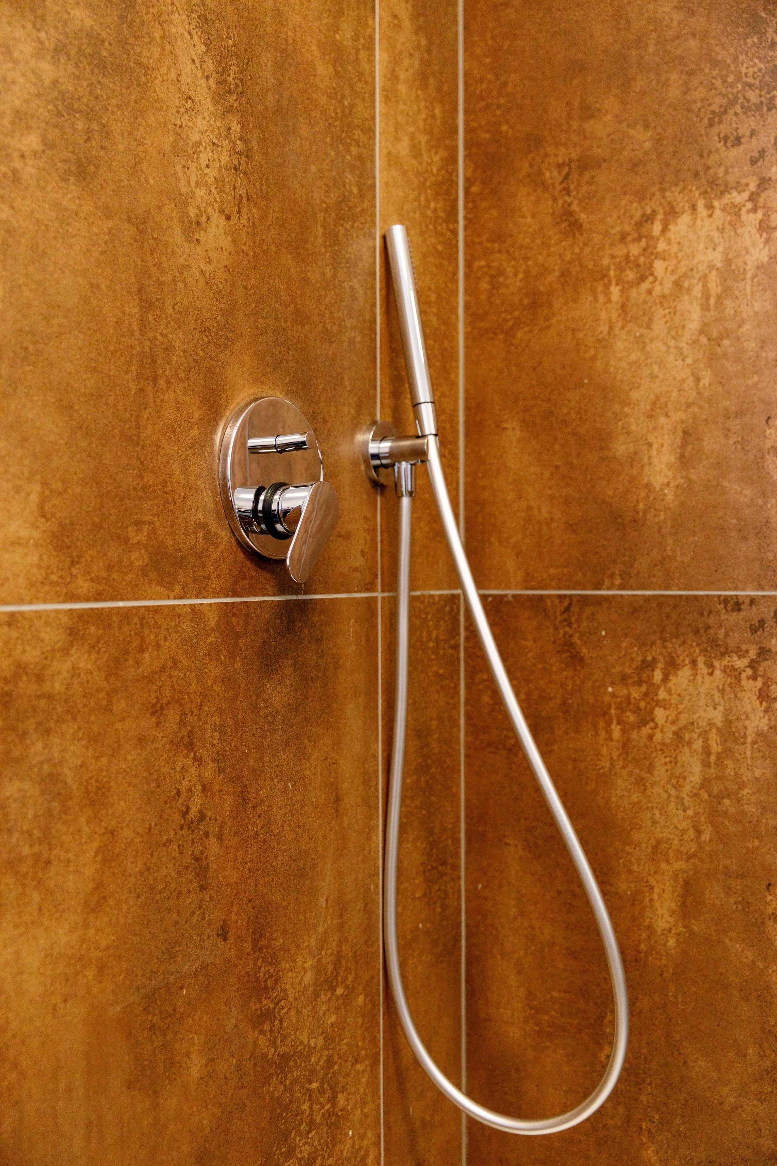 A shower with a chrome faucet and hose against a tiled wall.