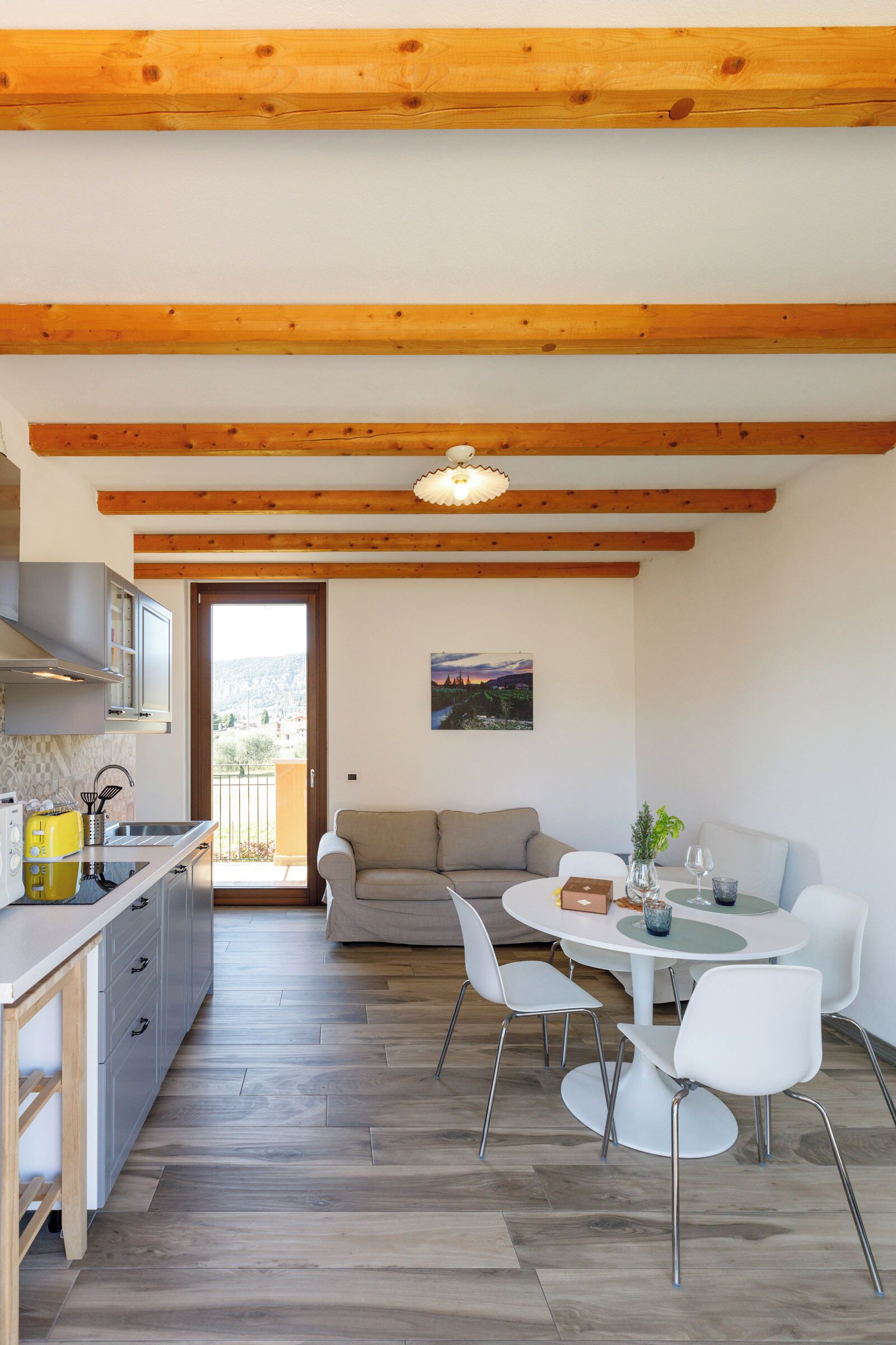 Une cuisine moderne avec des poutres en bois, un coin repas avec des chaises blanches et un canapé.