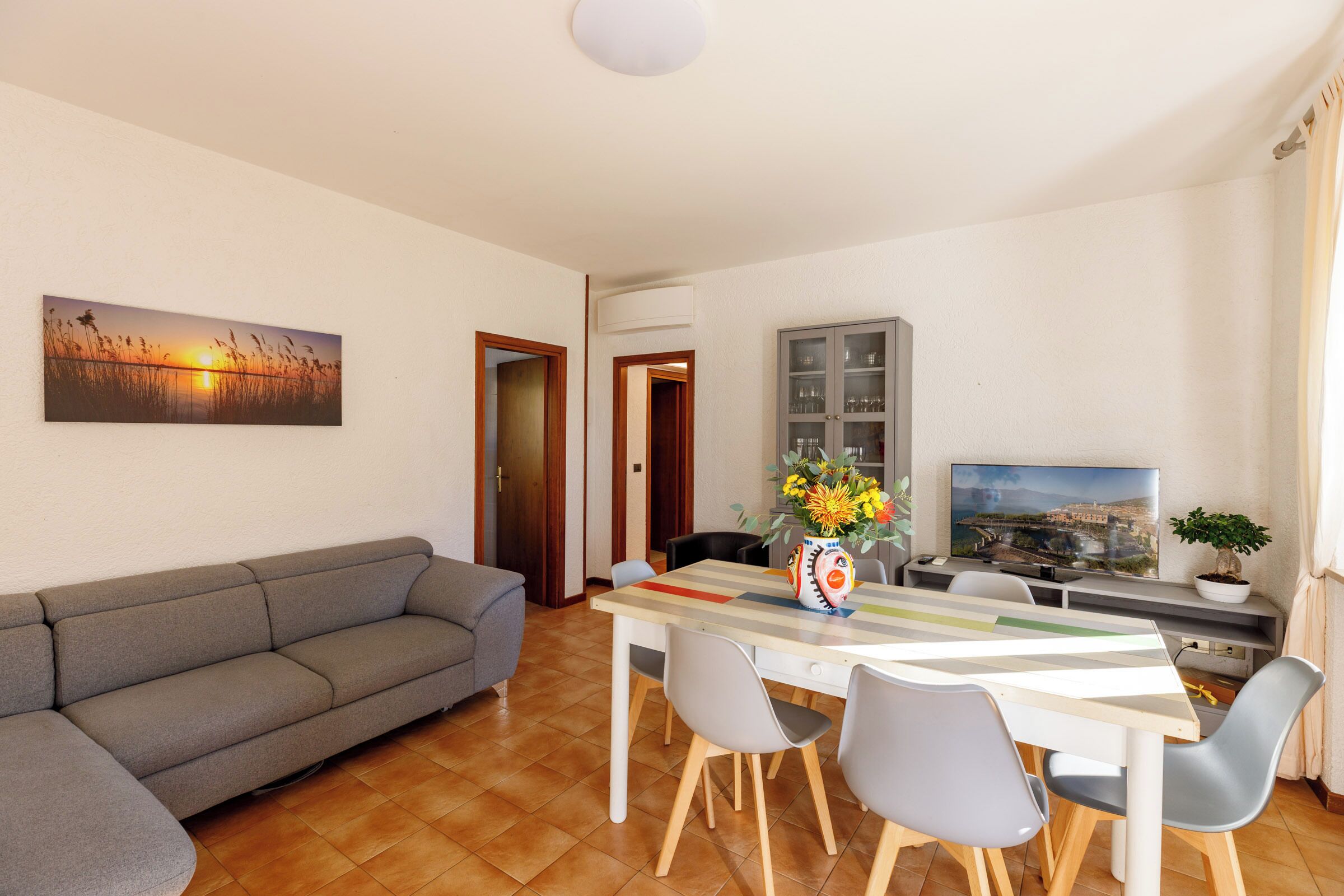 Una sala de estar con un sofá, una mesa de comedor con sillas, un televisor y un cuadro en la pared.