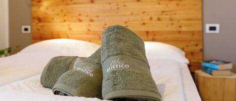 A bed with a wooden headboard and two rolled towels with the brand name "Rustico" on them.