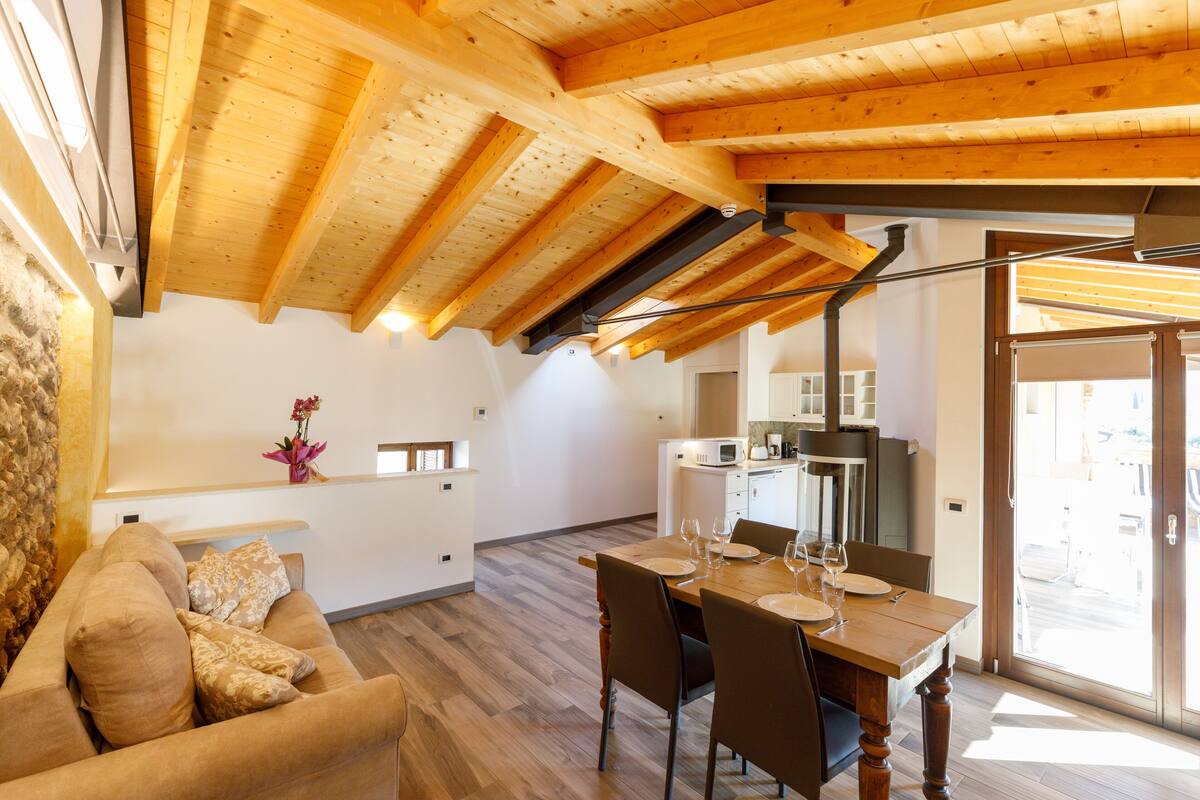A modern kitchen with wooden beams, a dining area with a wooden table and chairs, and a cozy living space with a sofa.