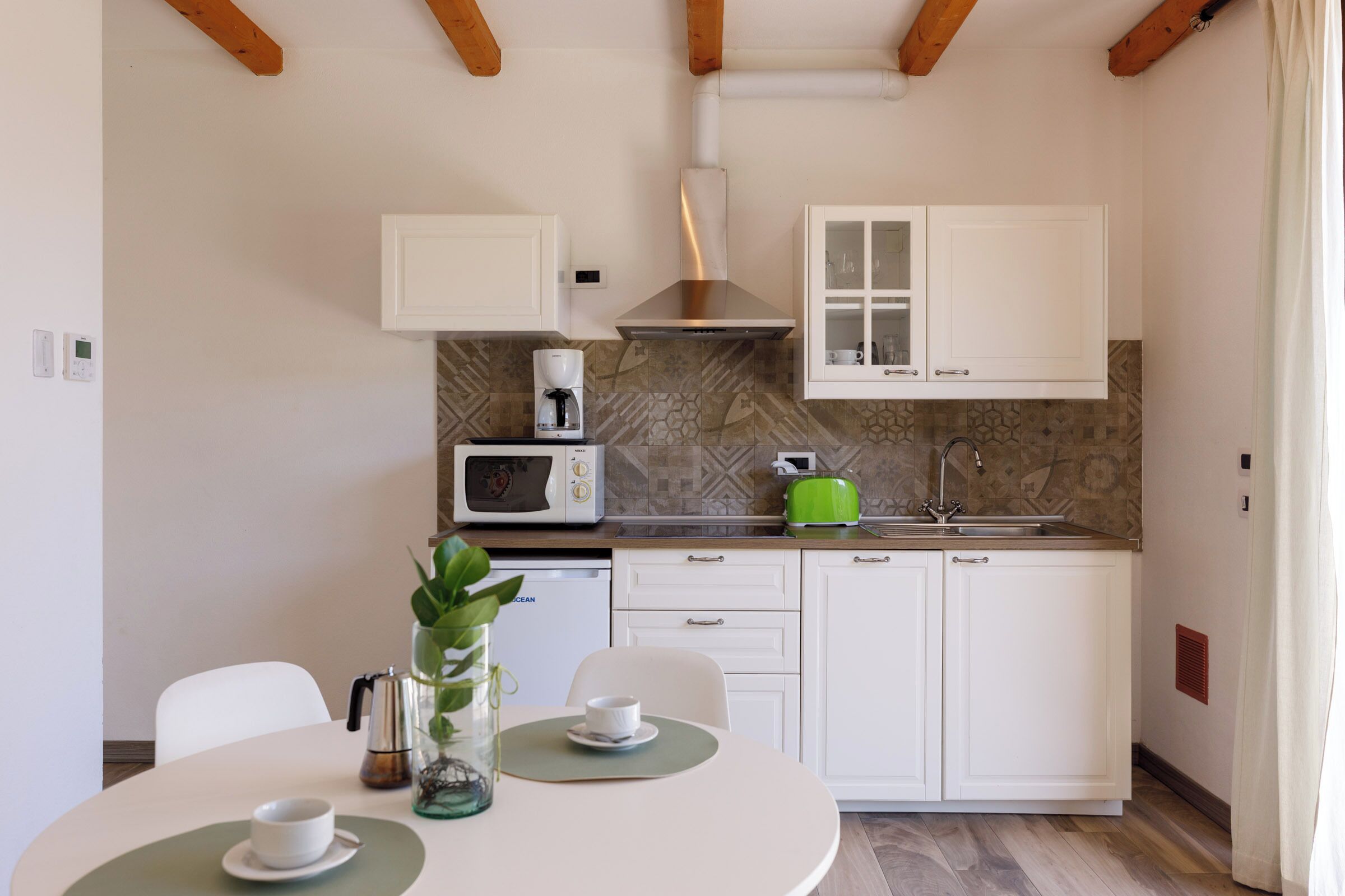 A compact kitchen with white cabinets, a microwave, a coffee maker, and a green toaster.