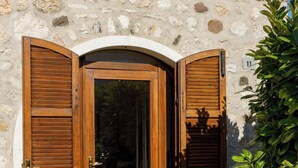 Un bâtiment en pierre avec une porte et des volets en bois, un sol carrelé et une enseigne portant le numéro « 11 ».