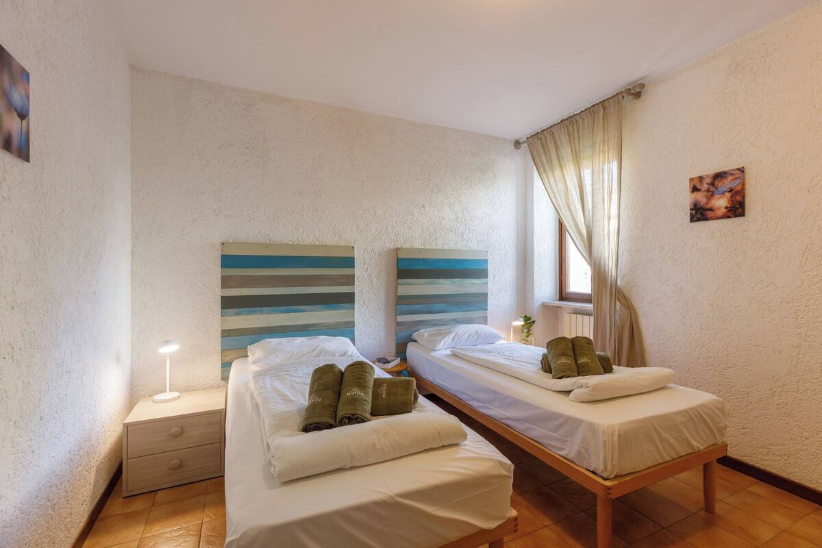 A room with two beds, a nightstand, and a window with curtains.