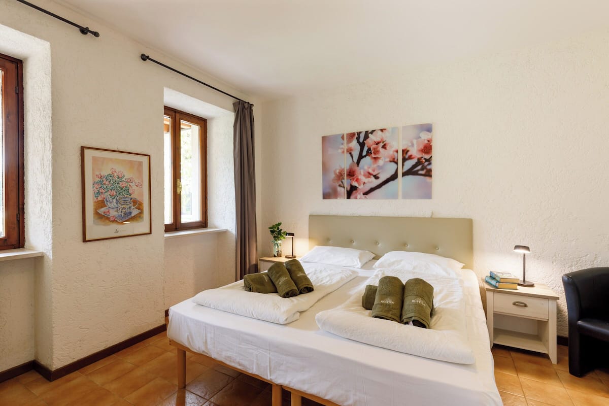 A hotel room with two beds, a nightstand with a lamp, a chair, and artwork on the walls.