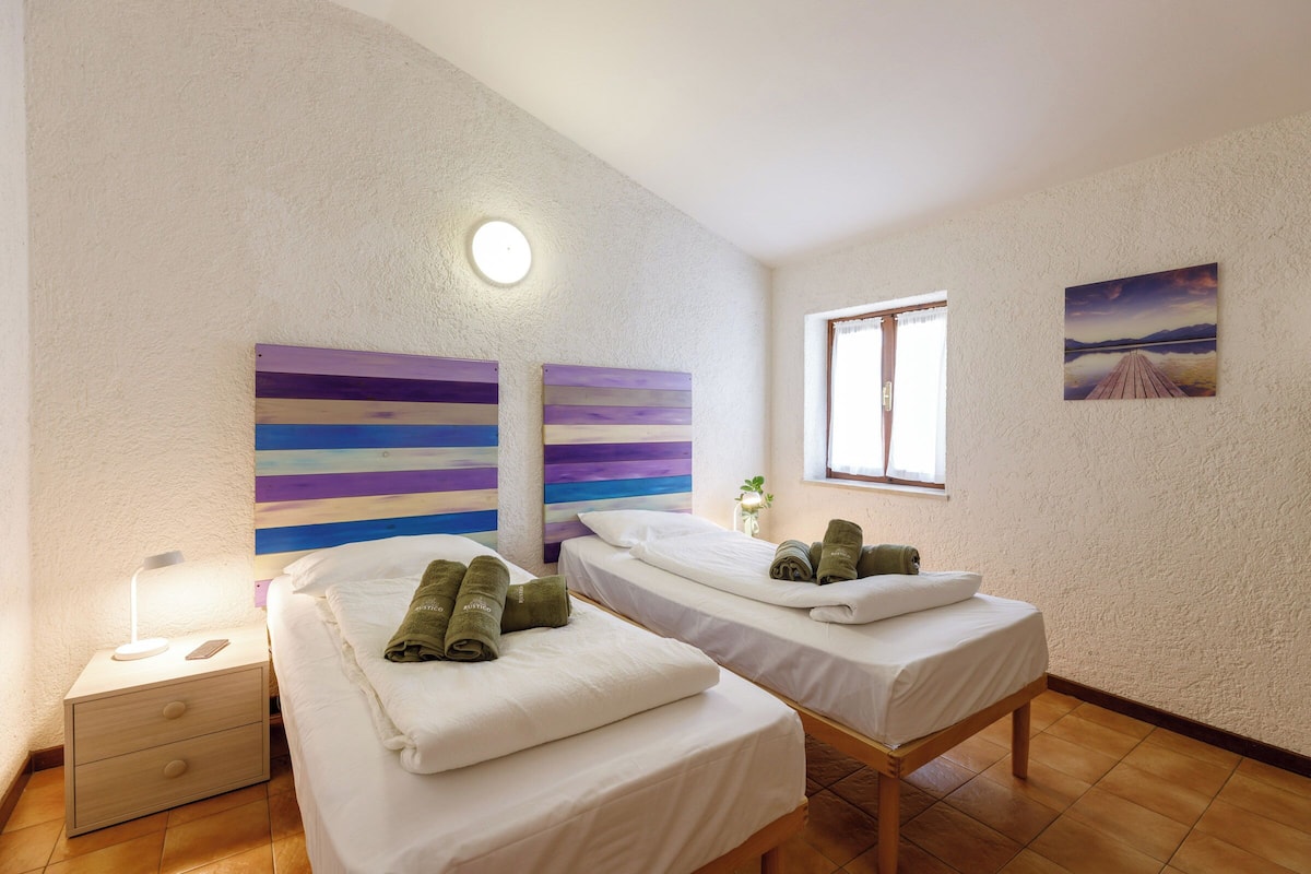 A room with two beds, a nightstand, a wall-mounted light, and a window with a view.