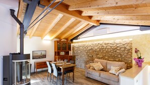Un salon chaleureux avec un mur en pierre, des poutres apparentes en bois au plafond, une cheminée, une table à manger avec des chaises et un canapé.