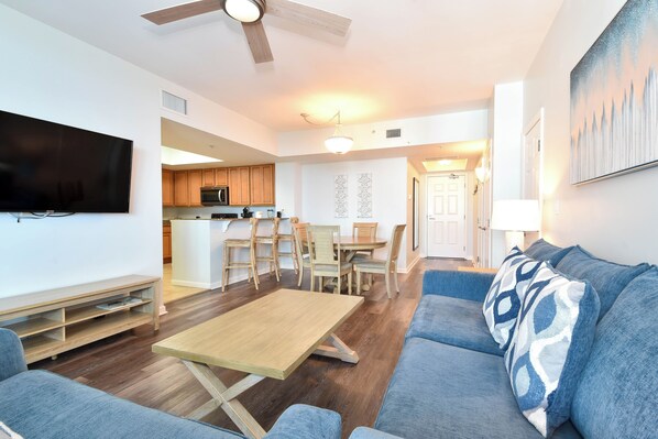 A modern living room with a wooden coffee table, blue sofa, and a flat-screen TV. - Beautiful, Updated 11th Floor Full Two Bedroom Condo at The Palms of Destin! (Destin)