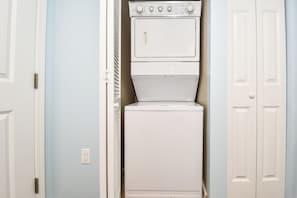 A laundry room with a stacked washer and dryer, white doors, and a light blue wall. - Gorgeous 12th Floor Views at The Palms of Destin! (Destin)