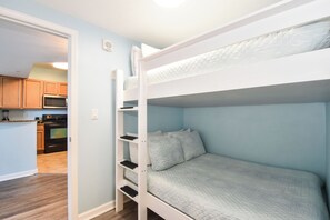 A bunk bed in a room with light blue walls, a kitchen area visible through an open door, and a white ceiling. - Gorgeous 12th Floor Views at The Palms of Destin! (Destin)