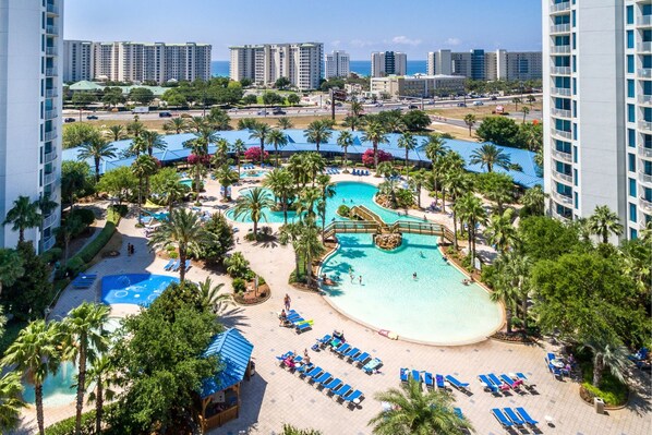 A resort with multiple swimming pools, palm trees, and a beach area with sun loungers.