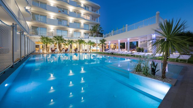 Un espace piscine d’hôtel comprenant une grande piscine, des chaises longues et un immeuble à plusieurs étages doté de balcons.