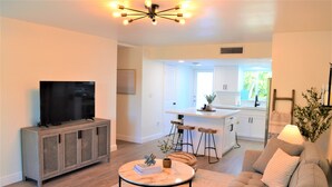 A modern living room with a flat-screen TV, a sofa, a coffee table, and a dining area with bar stools. - Newly renovated coastal home; Marina, Pools, Lagoon, Bikes, Tiki’s and More! (Key Largo)