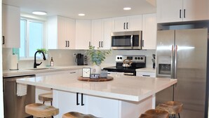 A modern kitchen with white cabinets, stainless steel appliances, and a central island with stools. - Newly renovated coastal home; Marina, Pools, Lagoon, Bikes, Tiki’s and More! (Key Largo)