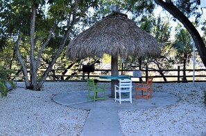 A thatched-roof structure with a table and chairs in a park setting.