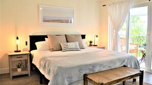 A bedroom with a bed, bedside tables, a bench, a window with curtains, and a view of the outdoors.