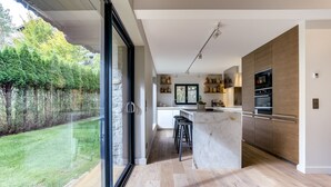 A modern kitchen with a large island, built-in ovens, and a view of a garden.