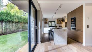 A modern kitchen with a large island, built-in ovens, and a view of a garden.