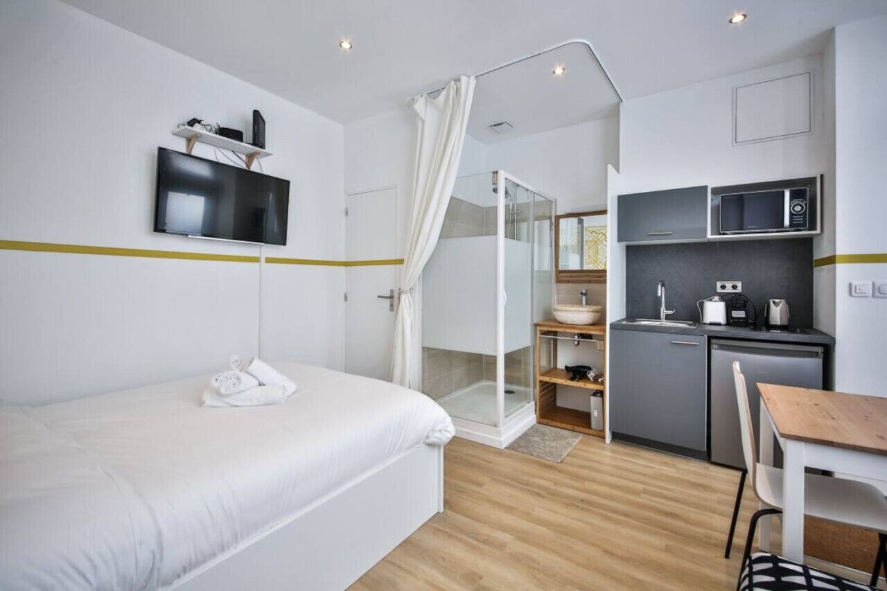 Moderni hotellihuone, jossa on sänky, televisio, suihku, pieni keittiö ja ruokailutila.