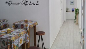 Un couloir d'hôtel avec une pancarte d'accueil, des tables recouvertes de nappes colorées et un escalier menant à un autre étage.
