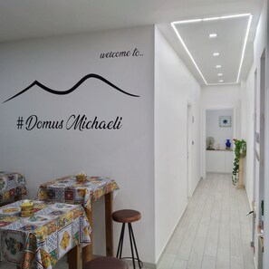 A hotel corridor with a welcome sign, tables with colorful tablecloths, and a staircase leading to another floor.