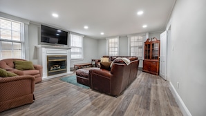A spacious living room with a fireplace, a television mounted above it, and a large wooden cabinet.