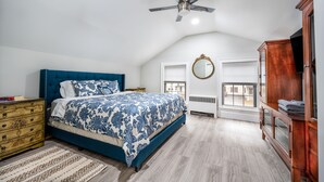 A bedroom with a blue bed, wooden dresser, and a ceiling fan.
