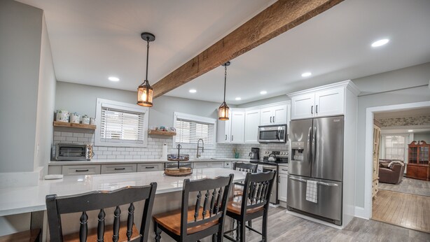A modern kitchen with white cabinets, a stainless steel refrigerator, a built-in microwave, and a wooden island with bar stools.