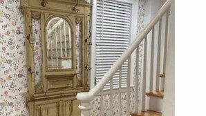 A staircase with a white railing and a wooden handrail, leading to a landing with a large, ornate mirror and a radiator.